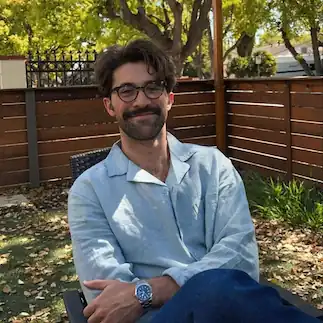 Portrait of a man with curly hair and tortoiseshell glasses, used as a face detected sample in an AI people search tool to identify and extract facial features for individual matching.